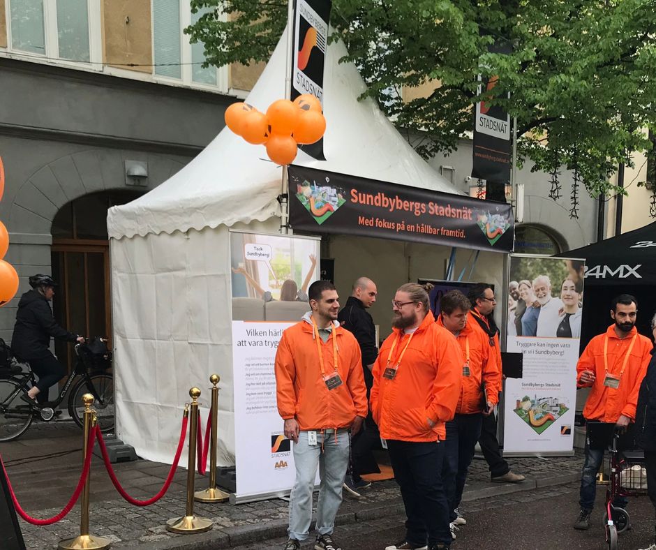 Anställda på Sundbybergs Stadsnät i orangea jackor utanför ett marknadstält.